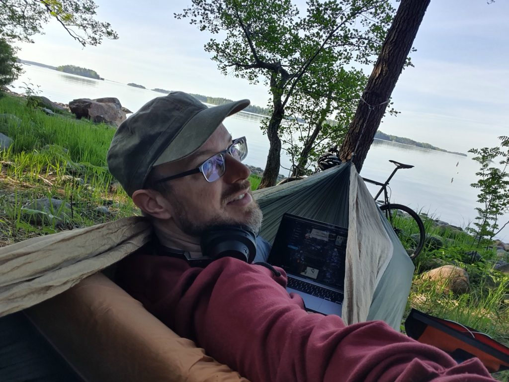 CTO Jaakko Alajoki riippumatossa etätyöpisteensä äärellä - järvenrannalla. Ottaa selfien.