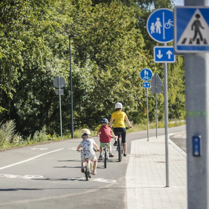 Kolme henkilöä pyöräilee kesäpäivänä