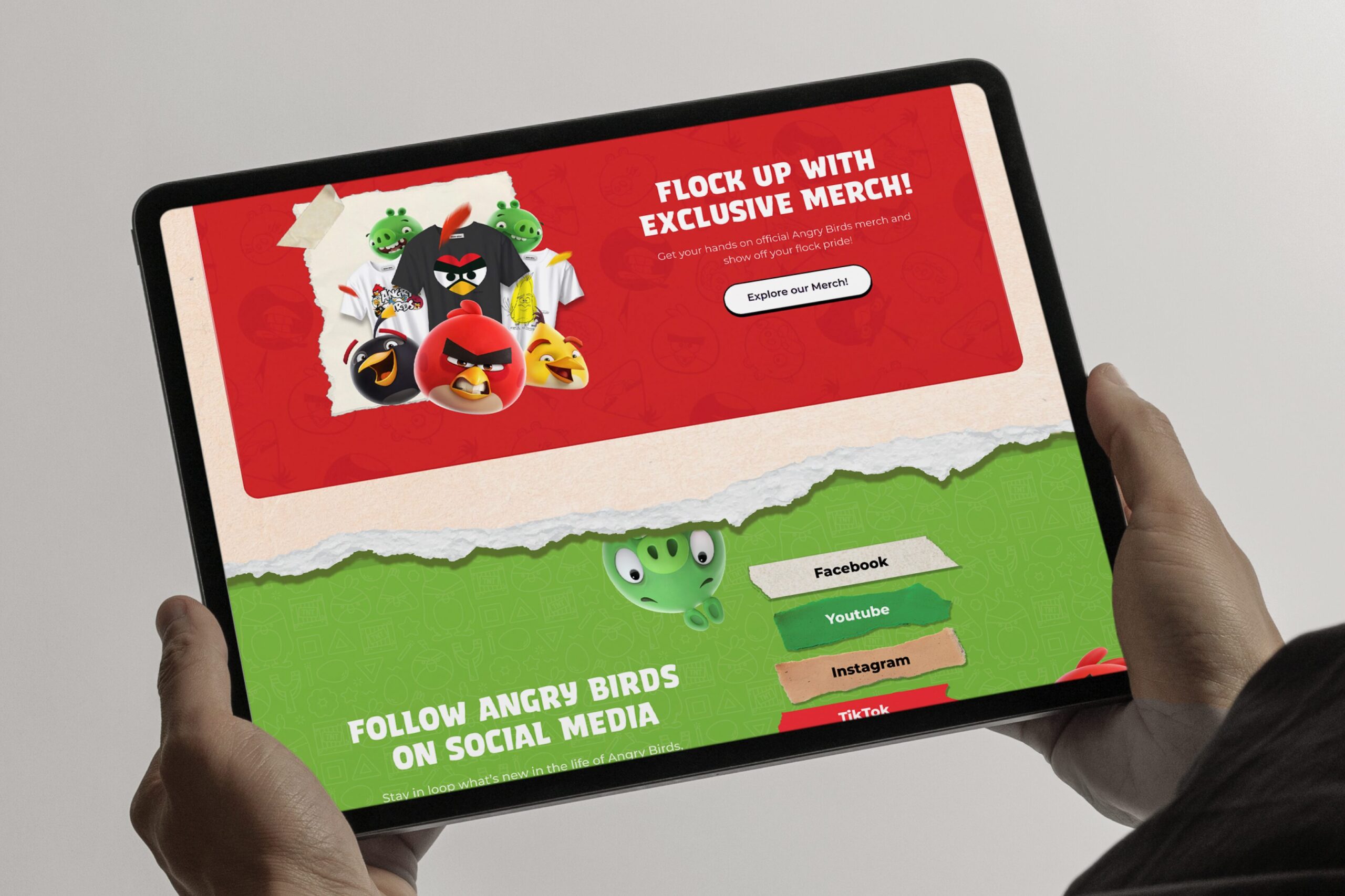 Kädet pitelevät tablettia, jossa näkyy Angry Birds -teemainen verkkosivu: punainen mainososio hahmoineen ja vihreä alaosa sosiaalisen median painikkeilla (Facebook, YouTube, Instagram, TikTok).