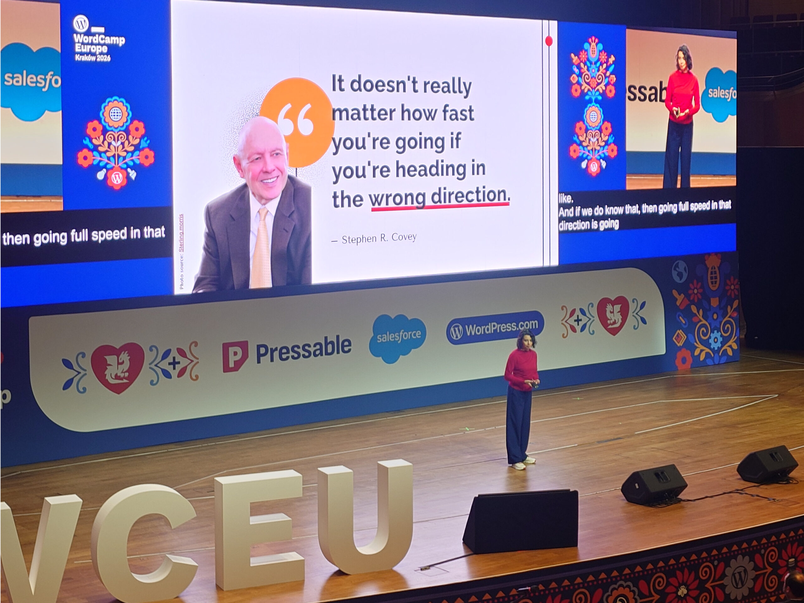Kuvassa WordCamp Europe 2026 -konferenssilava: esiintyjä seisoo lavalla punaisessa paidassa, taustalla suuri näyttö, jossa lainaus "It doesn't really matter how fast you're going if you're heading in the wrong direction." ja tapahtuman sponsorilogot, lavan etuosassa suuret VCEU-kirjaimet.