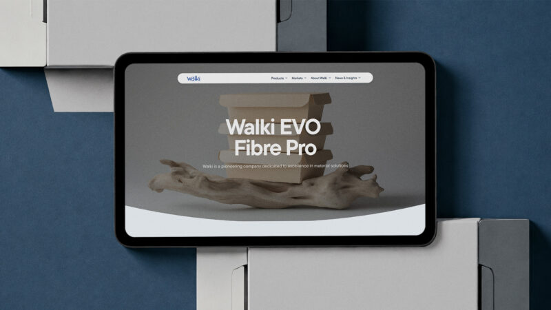 Tabletti avoinna Walki EVO Fibre Pro -verkkosivulla, näytöllä vaalea puunröykki ja otsikko; tabletti asetettuna valkoisten pakkauslaatikoiden päälle tummansiniselle taustalle.