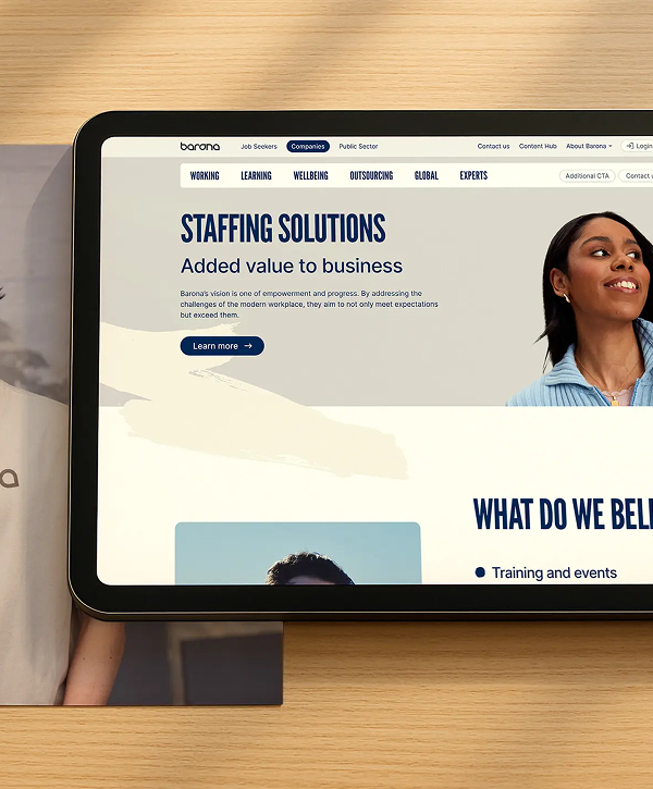 Tablet resting on a wooden surface showing the Barona website homepage with the headline "STAFFING SOLUTIONS — Added value to business," navigation links across the top, a blue "Learn more" button, and a smiling woman pictured on the right.
