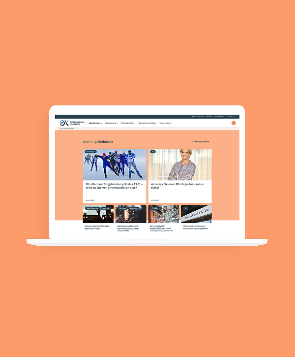 White laptop centered on a soft peach background showing the EK.fi website homepage with the EK logo at the top left, a horizontal navigation bar, and a main content area of headline article cards and image thumbnails in a grid.