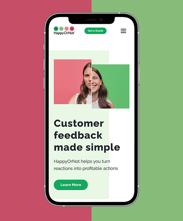 Smartphone mockup on a split red-and-green background showing the HappyOrNot mobile page with a composite portrait of a woman divided into color blocks, headline "Customer feedback made simple," subtext "HappyOrNot helps you turn reactions into profitable actions," and a green "Learn More" button.
