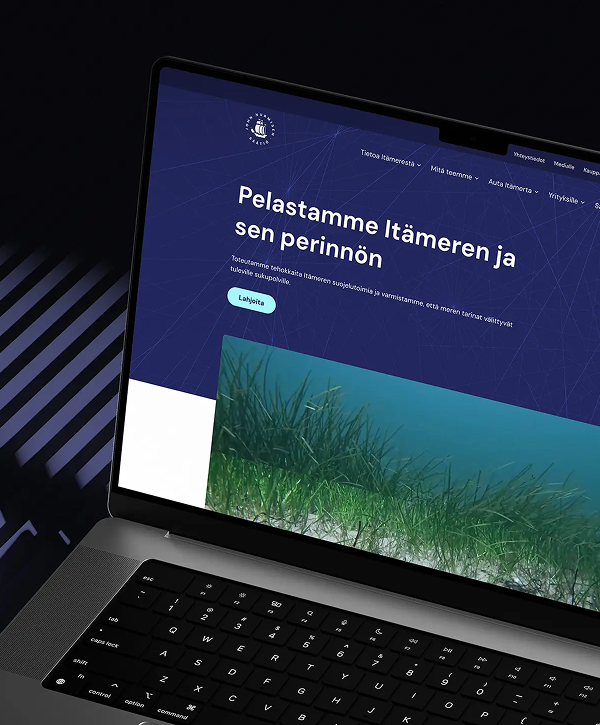 Close-up of a laptop on a dark surface displaying a Finnish-language website header that reads "Pelastamme Itämeren ja sen perinnön," a green call-to-action button and a large image of underwater seagrass.