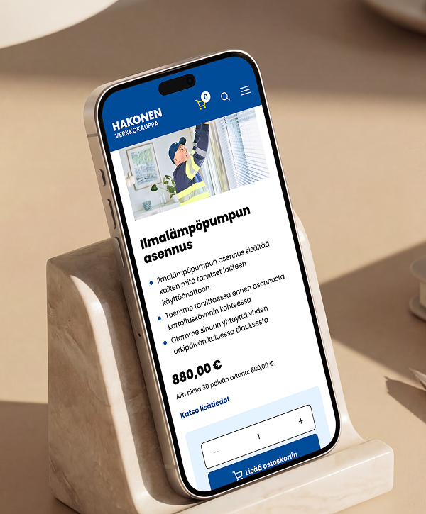 Close-up of a smartphone resting on a stone stand showing a Finnish Hakonen webshop product page titled "Ilmalämpöpumpun asennus" (air-source heat pump installation), with a small photo of a technician in a high-visibility vest, a short checklist of service details, the price "880,00 €" and an "add to cart" button under a blue site header.